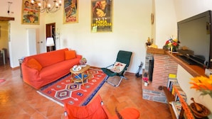A living room with a red sofa, a green armchair, and a television. There are posters on the wall and a fireplace. - Casa Palanca - Two Bedroom Villa, Sleeps 4 (Capannori)