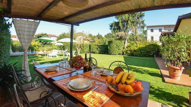 An outdoor dining area with a table set for two, surrounded by greenery and a view of a swimming pool and garden. - Casa Palanca - Two Bedroom Villa, Sleeps 4 (Capannori)