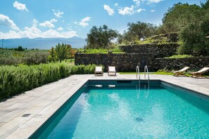 Une piscine avec des chaises longues, un mur en pierre et une vue sur les montagnes.