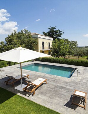 Une piscine avec un parasol, des chaises longues et une petite table.