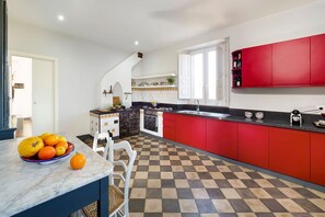 A kitchen with red cabinets, a checkered floor, and a marble countertop with fruit.