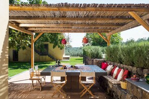 An outdoor dining area with a pergola, a table with chairs, and a stone wall with cushions.