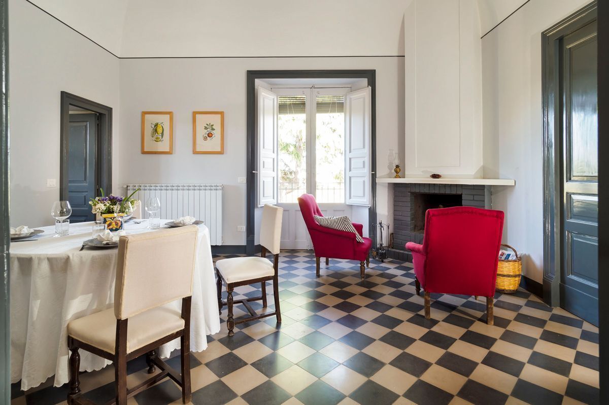 Un coin repas avec un sol à carreaux, une cheminée et un fauteuil rouge.