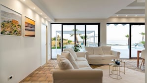 A modern living room with a beige sofa, a coffee table, and a view of the sea through large windows. - Cella Mimavi - Three Bedroom Villa, Sleeps 6 (Ribera)
