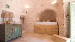 Une pièce rustique avec un mur en pierre, un lit en bois, une armoire verte et un banc.