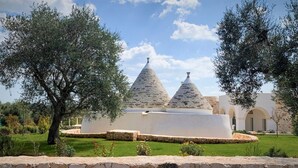 Un bâtiment aux murs de pierre, surmonté de deux toits coniques, entouré d’une pelouse bien entretenue et d’arbres.