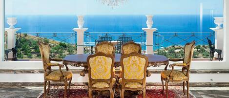 A dining area with a table and chairs, a chandelier, and a view of the ocean.