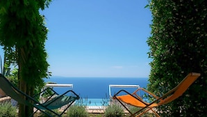 Two lounge chairs facing a pool with a view of the sea.