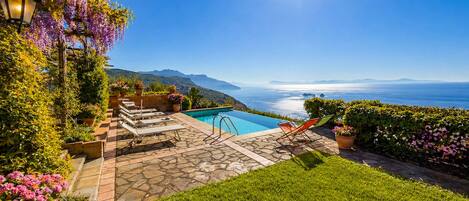 A pool area with a clear view of the ocean and mountains.