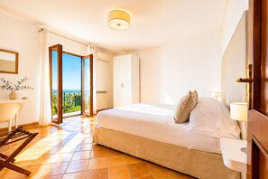 A bedroom with a bed, a desk, a chair, a wardrobe, and a view of the outdoors.