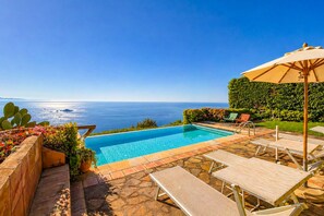 Ein Pool mit Blick auf den Ozean, umgeben von Liegestühlen und einem Sonnenschirm.