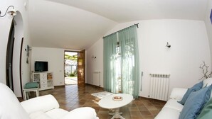 A spacious living area with a white sofa, a small table, and a television on a cabinet.