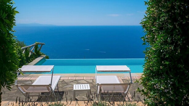 A poolside area with lounge chairs and a view of the ocean.