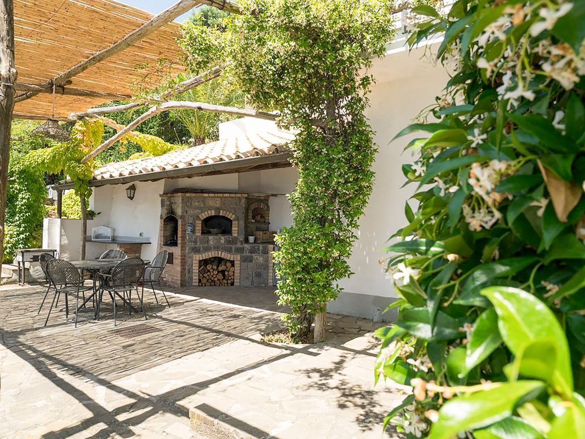 Une terrasse extérieure dotée d’une cheminée en pierre, d’une table à manger avec des chaises et d’une pergola offrant de l’ombre.