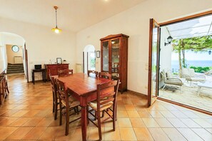A dining area with a wooden table and chairs, a cabinet with glass doors, and a view through a glass door to an outdoor seating area.