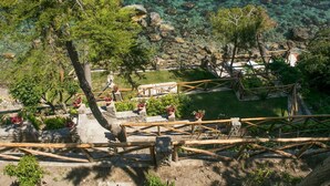 Un jardín en terrazas con muros de piedra y pasarelas de madera, con vistas a un lago azul y despejado donde se ven rocas.