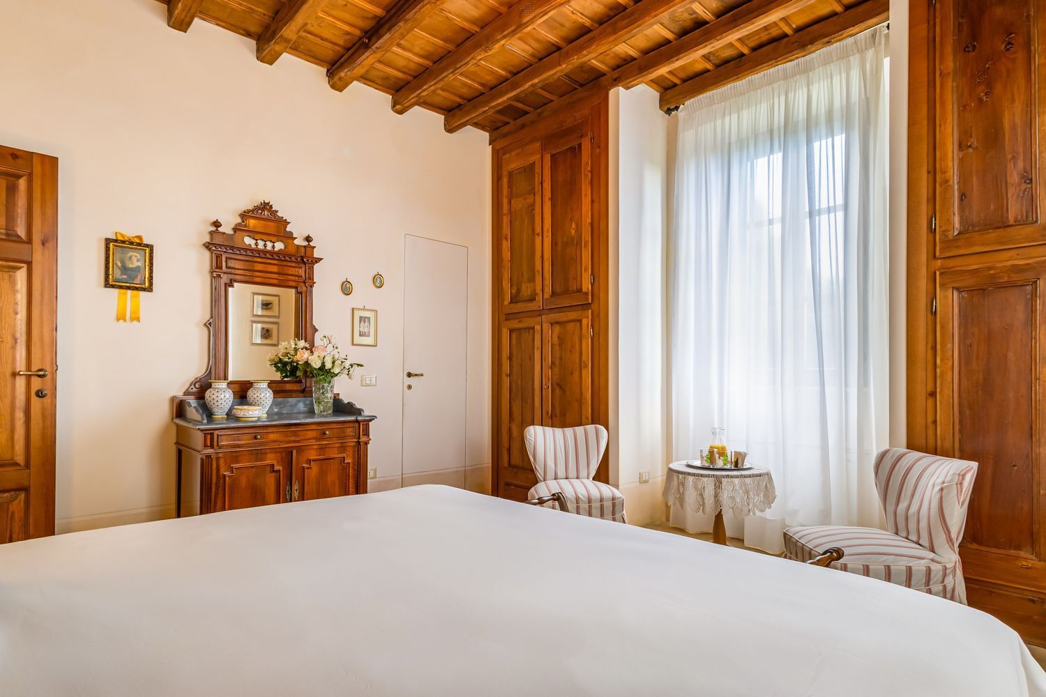 Une chambre à coucher avec un grand lit, une armoire en bois, une coiffeuse avec un miroir et deux chaises.