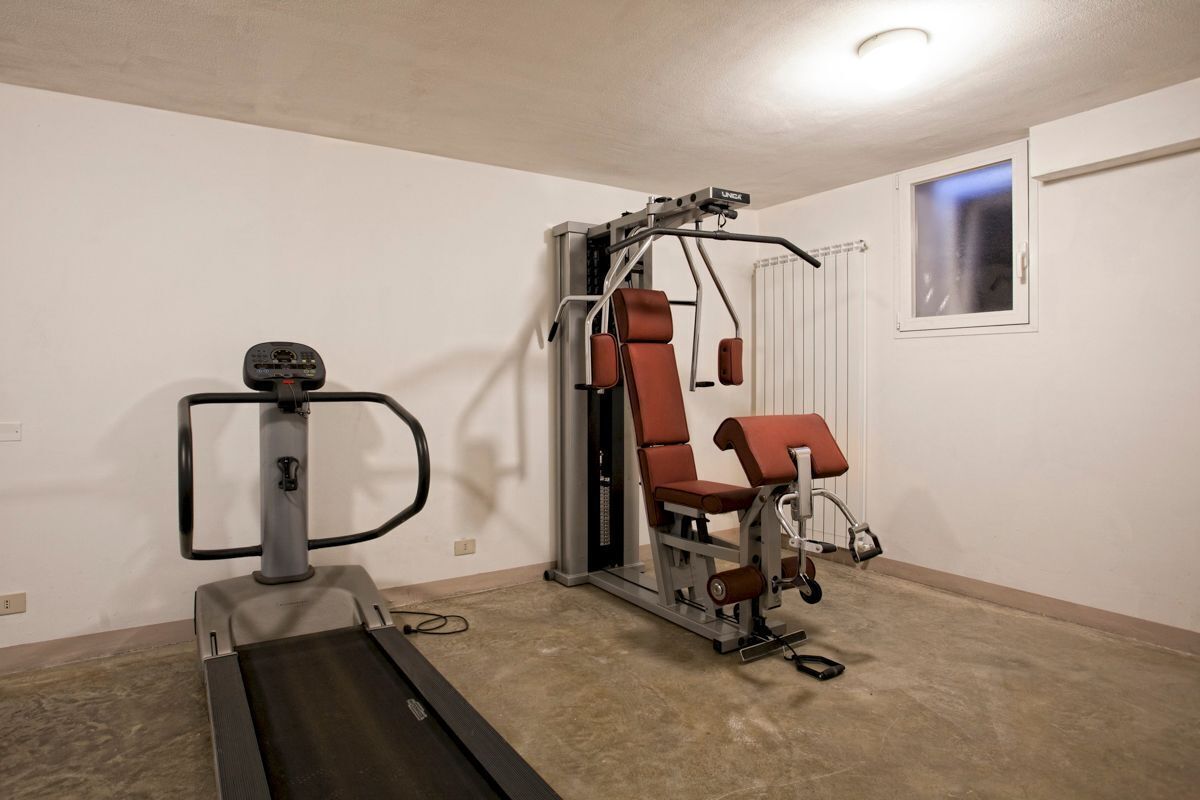 Ein Heimfitnessraum mit Laufband, Multifunktionsgerät und einem Fenster.