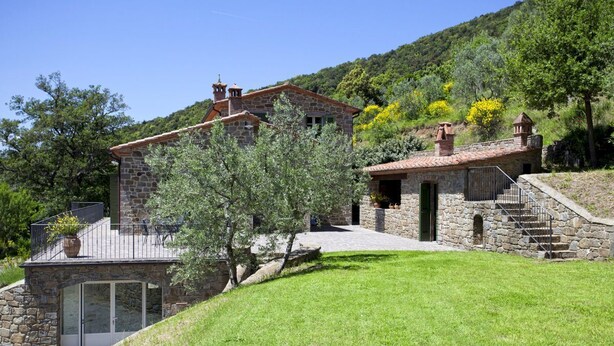 A stone house with a patio, a staircase, and a view of the surrounding greenery.