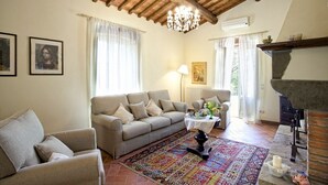 A living room with a sofa, armchairs, a patterned rug, a chandelier, and a fireplace.