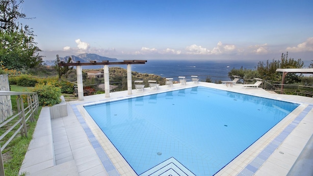 Una piscina rectangular con agua cristalina azul, rodeada por un solado de baldosas y una pérgola de madera.
