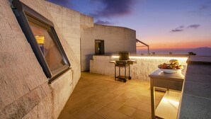 Terraza en la azotea con área de parrillada y mesa con comida, con vista a un atardecer.