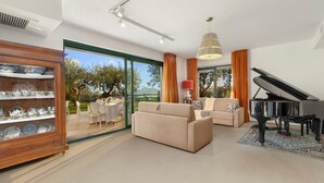 Una sala de estar moderna con un piano, un sofá y un comedor con un aparador de vidrio.