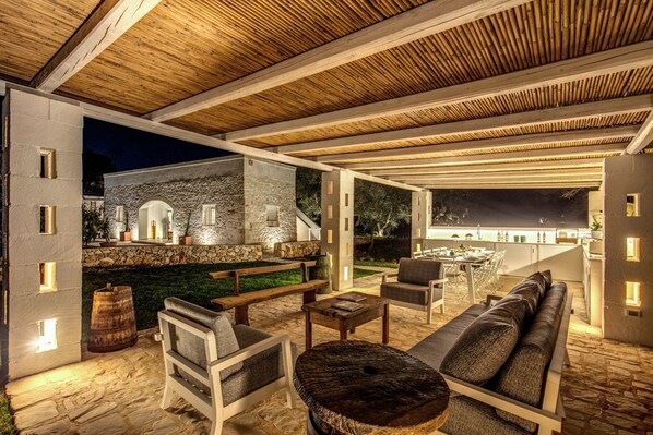 An outdoor patio area with stone flooring, wooden furniture, and a stone wall backdrop.