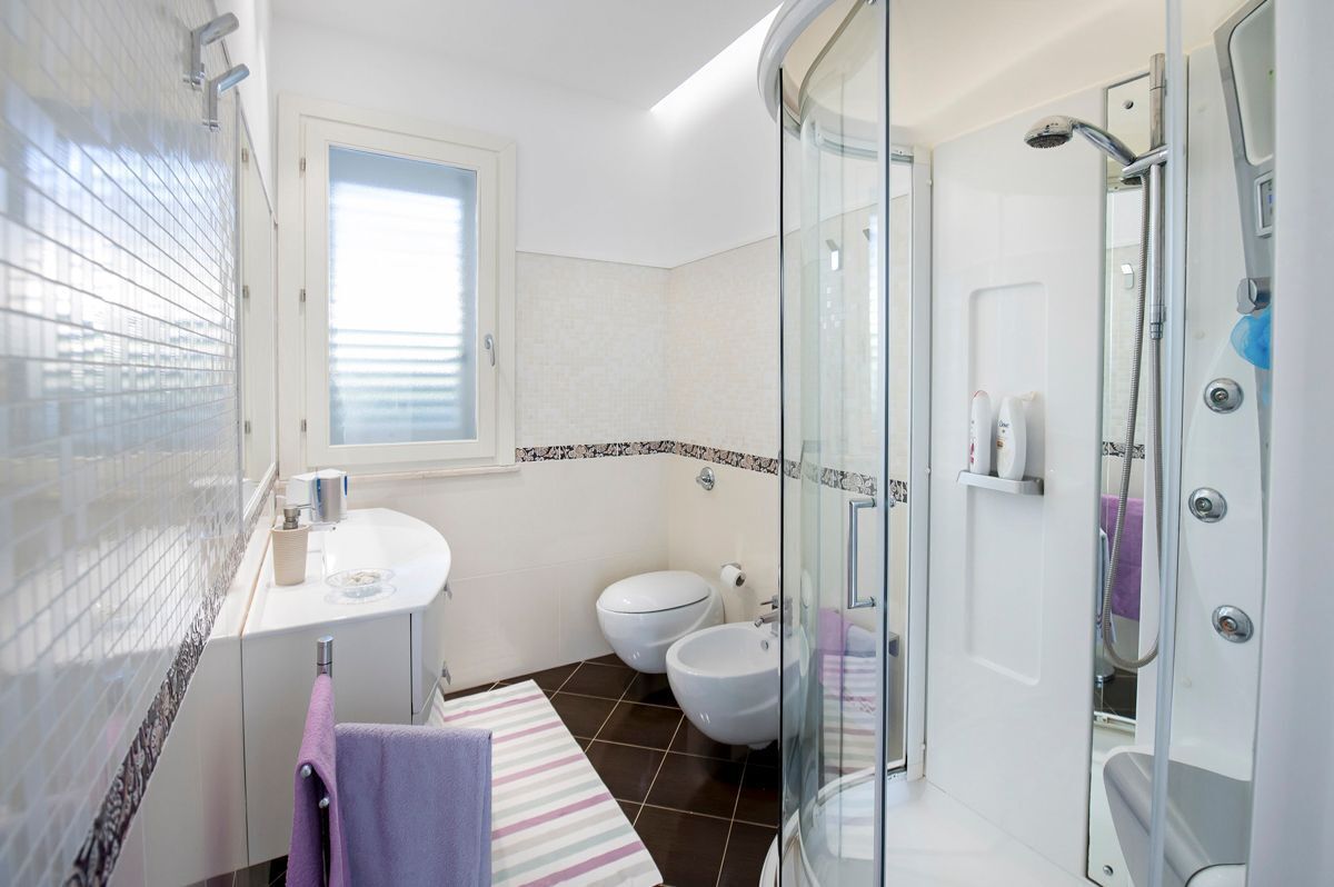Un baño moderno con cabina de ducha de vidrio, un lavabo blanco y un bidé.