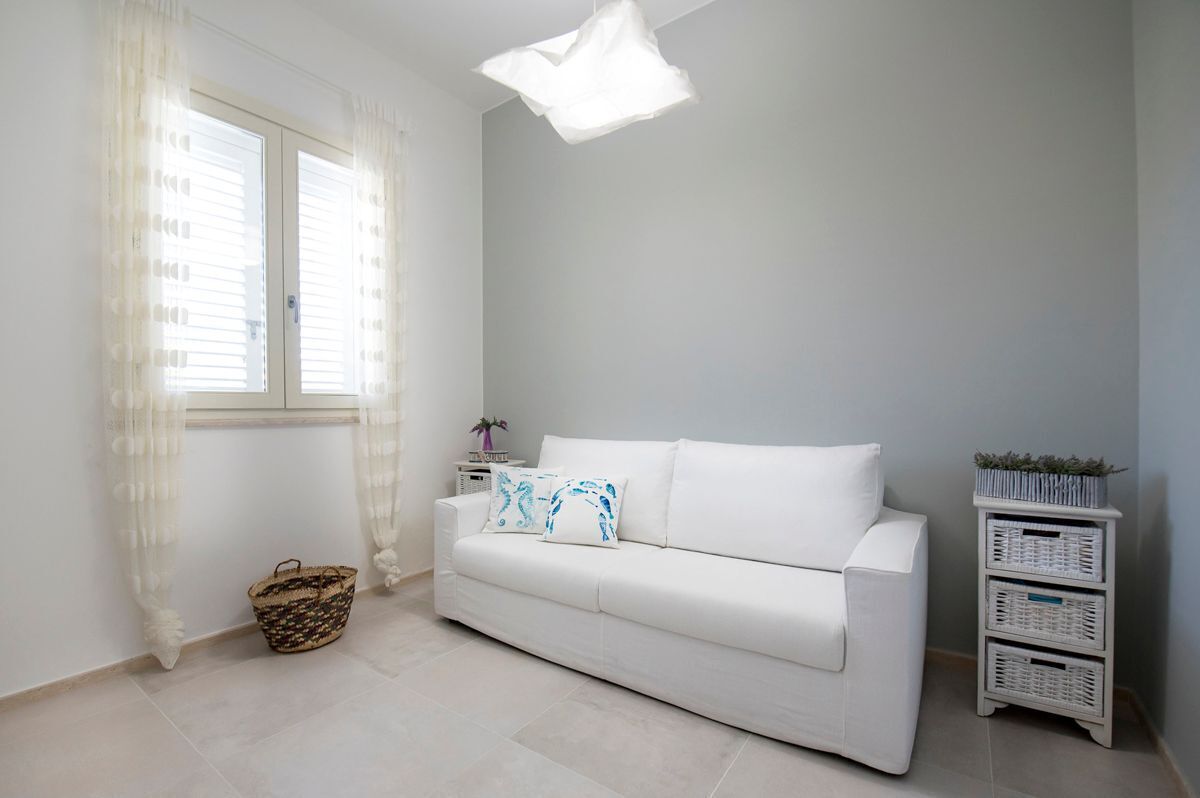 Un canapé blanc avec deux coussins, un panier blanc et une petite table d’appoint blanche sur laquelle est posée une plante.