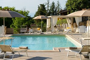 A pool area with lounge chairs and umbrellas, surrounded by greenery and a stone building.