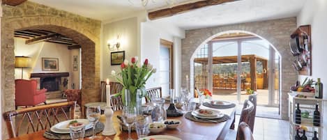 A dining area with a stone archway, wooden beams, and a view to the outside.