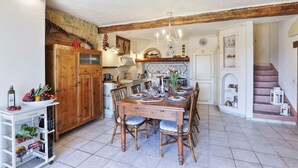 Una cocina rústica con vigas de madera, una mesa de comedor preparada para cuatro personas y un armario blanco con puertas de vidrio.