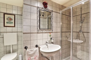Une salle de bain avec un lavabo blanc, une cabine de douche en verre et un miroir orné d’une rose rouge.