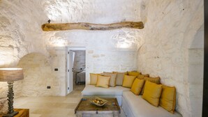 A cozy interior with a stone wall, a wooden beam ceiling, a white sofa with yellow cushions, a wooden coffee table, and a lamp. - Trulli Daniele - Three Bedroom Villa, Sleeps 6 (Locorotondo)