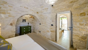 A stone-walled room with a bed, a green dresser, and an arched doorway leading to an outdoor area. - Trulli Daniele - Three Bedroom Villa, Sleeps 6 (Locorotondo)