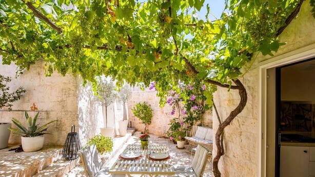 A sunlit patio with a table and chairs, surrounded by potted plants and a stone wall. - Trulli Daniele - Three Bedroom Villa, Sleeps 6 (Locorotondo)