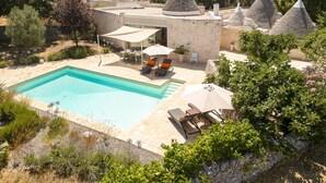 A pool area with lounge chairs and umbrellas, surrounded by stone buildings with conical roofs. - Trulli Daniele - Three Bedroom Villa, Sleeps 6 (Locorotondo)
