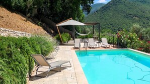 Una piscina con sillas de descanso y una hamaca, rodeada de follaje y montañas al fondo.