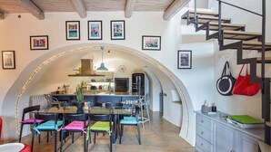 Un comedor con una isla central, sillas con cojines de colores y una cocina al fondo.