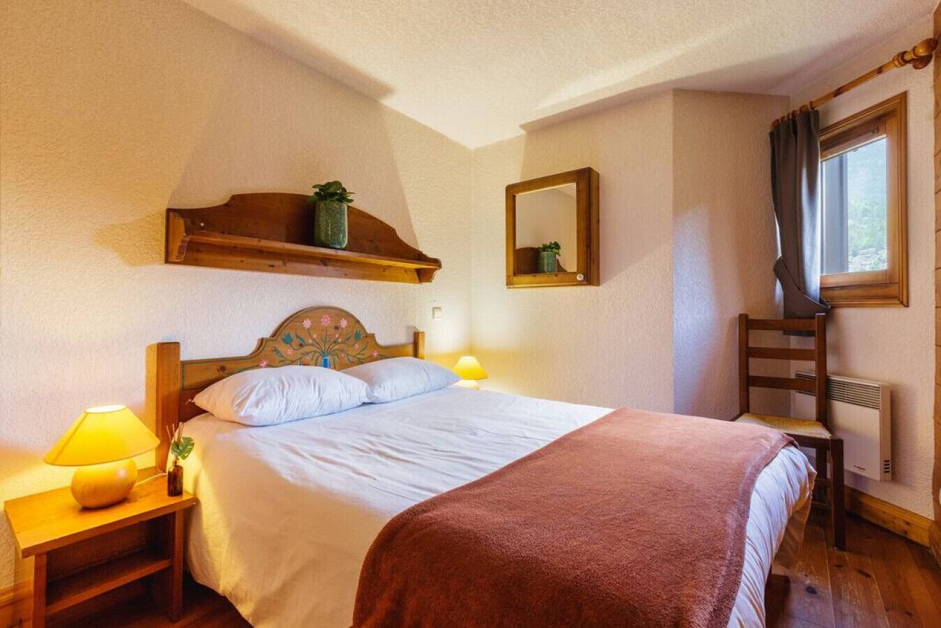 Une chambre à coucher avec un lit, des tables de chevet, un miroir et une fenêtre avec des rideaux.