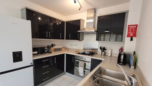 A modern kitchen with black cabinets, a stainless steel sink, a built-in oven, and a microwave. - House of 4 Chimneys by Your Lettings UK (Peterborough)