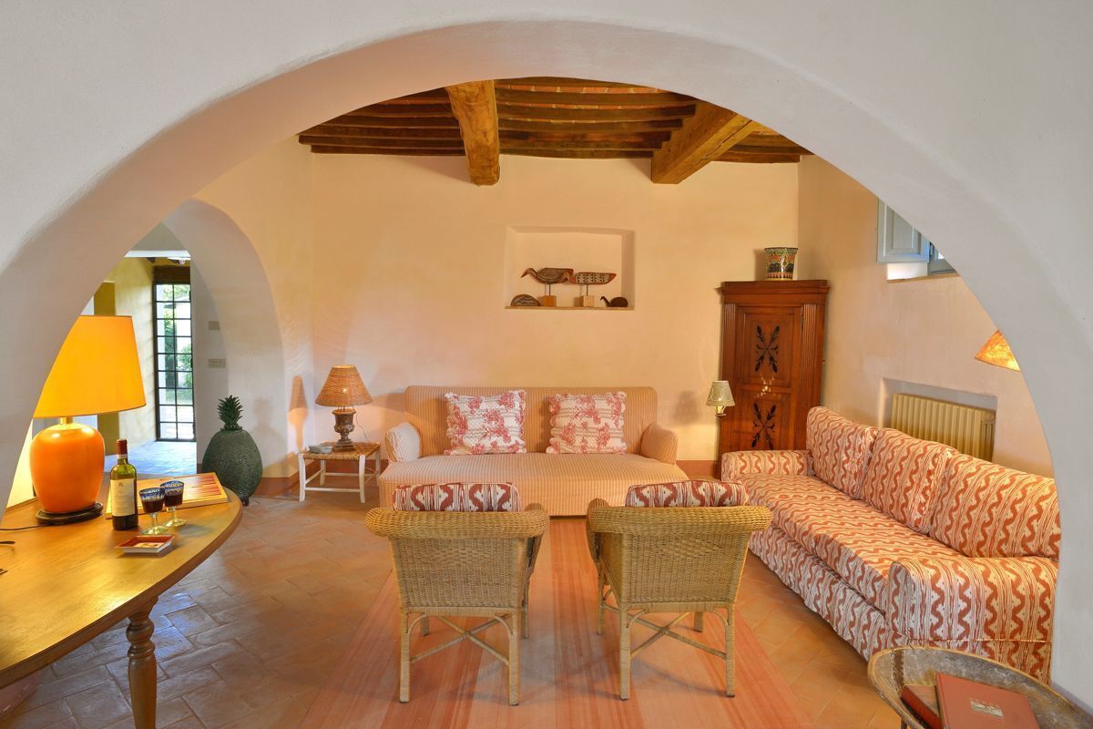 Une pièce chaleureuse avec un plafond en bois, un canapé, deux fauteuils en osier, une table avec une lampe et un buffet.