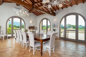 A dining room with a large wooden table surrounded by chairs, large arched windows, and a chandelier. - I Tebaldi - Eight Bedroom Villa, Sleeps 18 (Reggello)