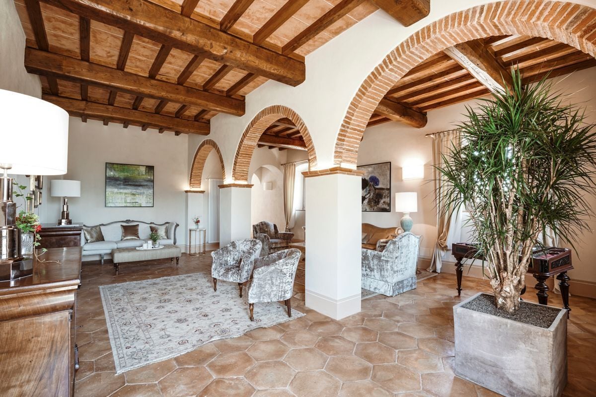 A spacious living area with a high ceiling, exposed wooden beams, and a large potted plant.