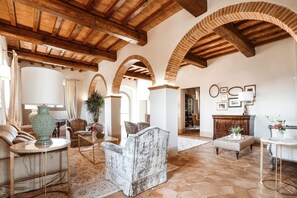 A spacious living area with a high wooden ceiling, arched brick columns, and a mix of furniture including sofas, a coffee table, and a side table. - I Tebaldi - Eight Bedroom Villa, Sleeps 18 (Reggello)