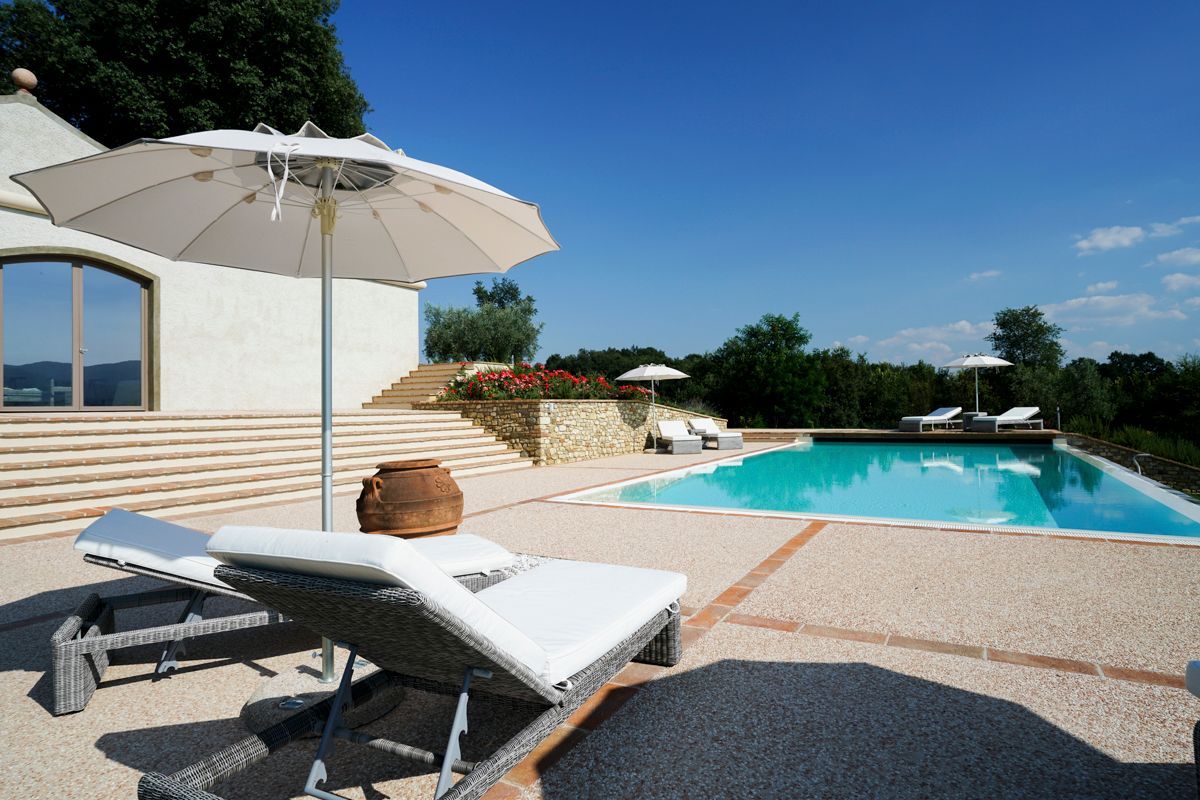 Un espace aménagé au bord de la piscine, avec des chaises longues, un grand parasol et un mur de pierre doté de marches menant à la piscine.