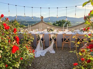 An outdoor dining area with tables set for a meal, surrounded by red roses and a mountainous backdrop. - I Tebaldi - Eight Bedroom Villa, Sleeps 18 (Reggello)