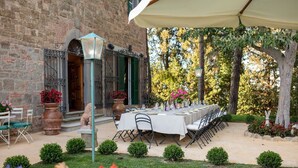 An outdoor dining area with a long table set for a meal, surrounded by greenery and a brick building. - Tenuta Bartolucci - Ten Bedroom Villa, Sleeps 22 (Palaia)