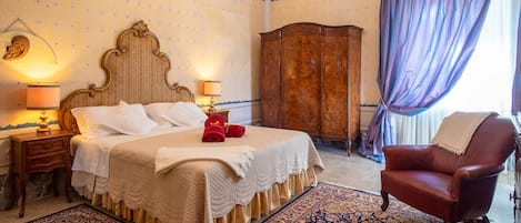A hotel room with a large bed, a wooden wardrobe, a leather armchair, and a chandelier.